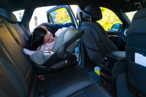 Mother fastening carseat to prevent injuries in accidents. Common injuries suffered by children in car accidents.