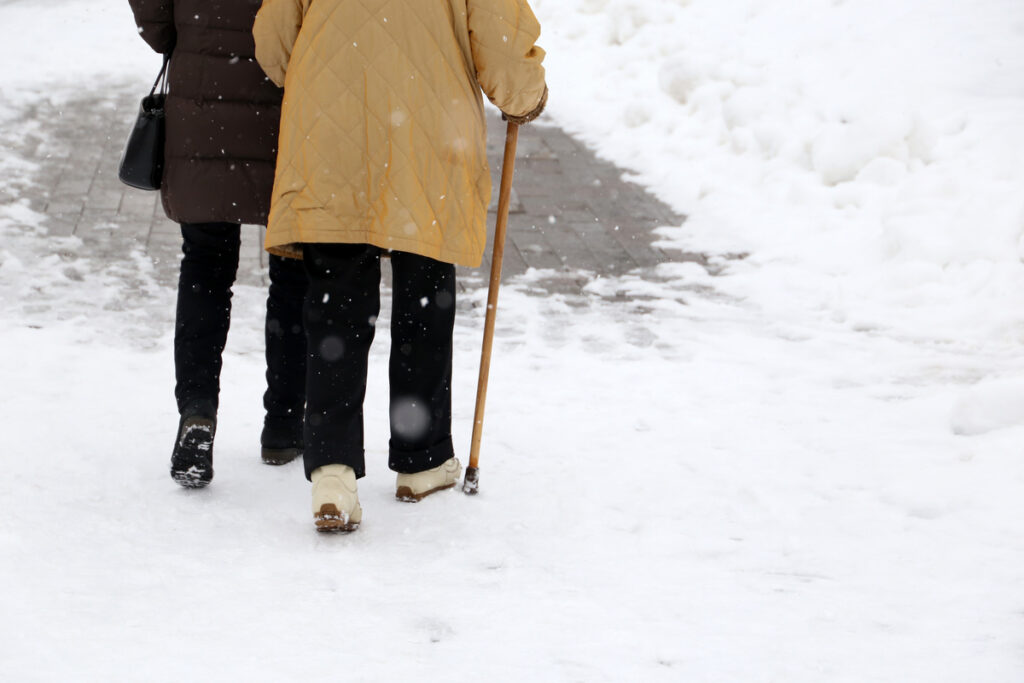 Woman walking with a cane during snowfall. Concept of limping, old age, winter weather, elderly or blind person