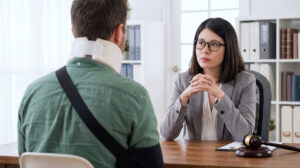 Woman lawyer consulting with injured client wearing neck brace in modern office setting with bookshelves and natural light Woman lawyer consulting with injured client wearing neck brace in modern office setting with bookshelves and natural light