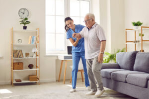 Smiling caregiver helping senior man to stand up and walk. Female nurse assisting her elderly patient suffering from mental disability in nursing home. Disabled old man trying to walk with assistance Smiling caregiver helping senior man to stand up and walk. Female nurse assisting her elderly patient suffering from mental disability in nursing home. Disabled old man trying to walk with assistance
